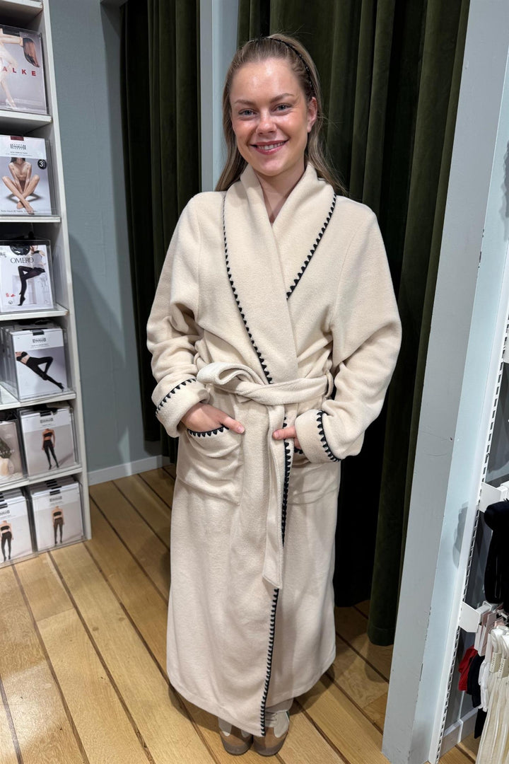 Pluto Quinta lang morgenkåpe i beige fleece med svarte kontrastdetaljer på krage og mansjetter.